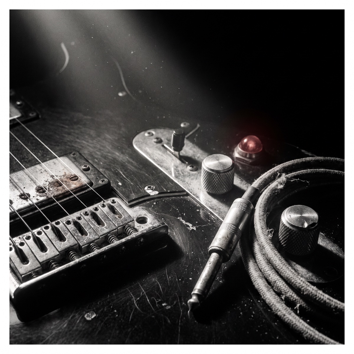 Close-up of a worn electric guitar bridge and pickups beside scratched amplifier knobs, a coiled cable and a single red pilot lamp