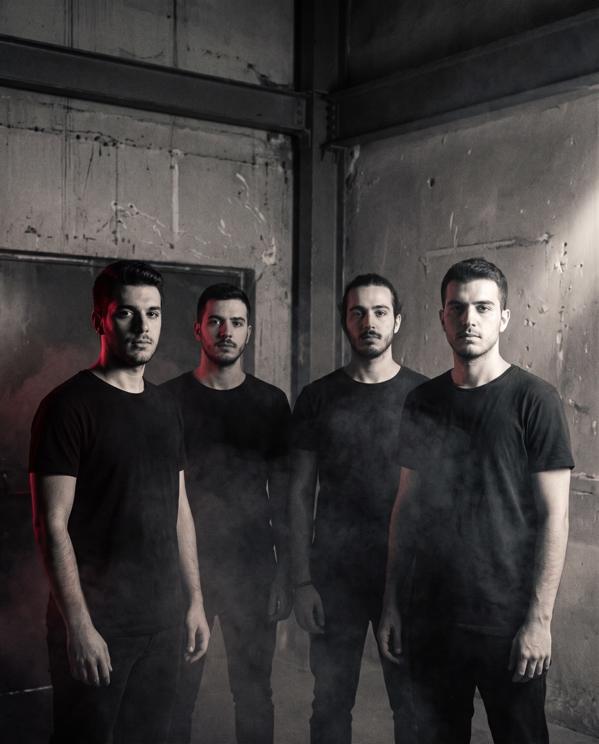 Editorial portrait of the four members of Apotypomata standing in a dark industrial space, hard side light, smoke drifting across them